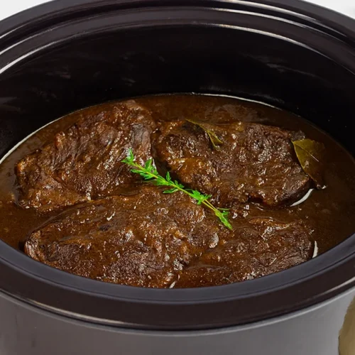 Vier stukjes draadjesvlees in de slowcooker met een takje groen en een laurierblaadje.