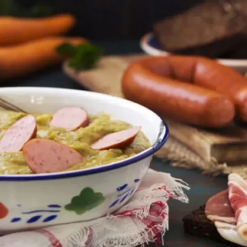 Erwtensoep recept van oma in een ouderwets kommetje met rookworst en plakjes spek ernaast.