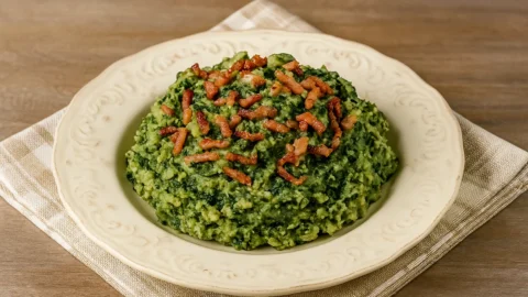 Oma's spinazie stamppot met spekjes op een wit bord met een ouderwets doekje eronder.